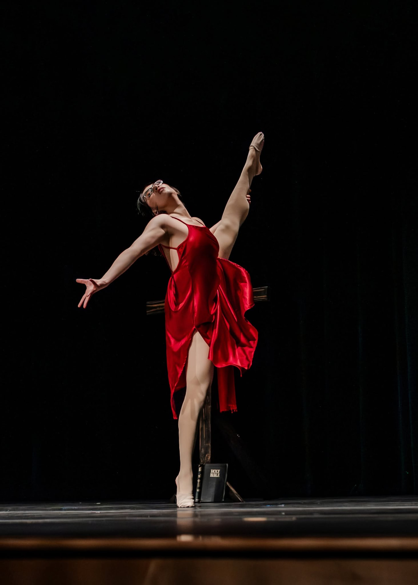 Senior dancer in a red dress in a high extension on stage