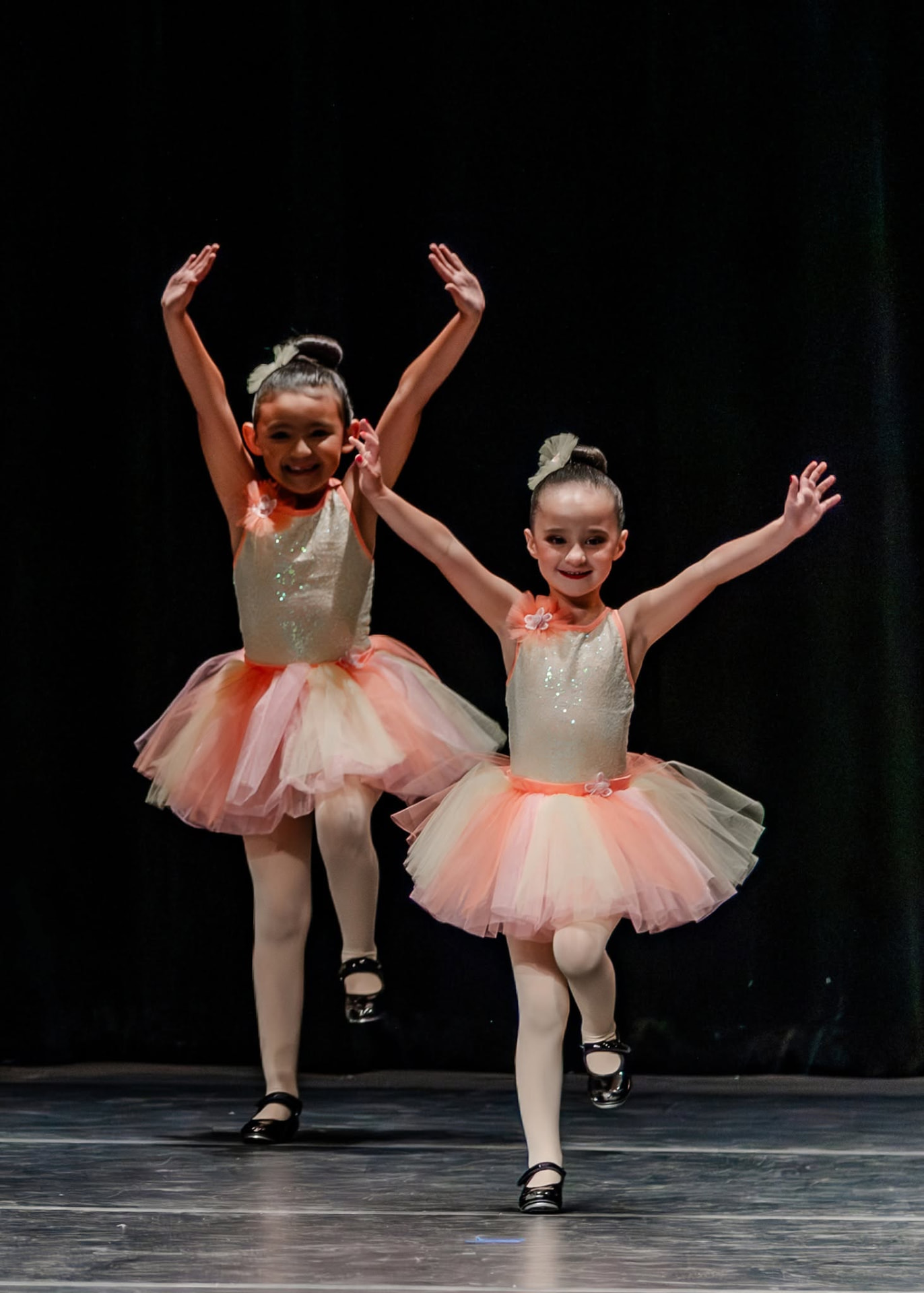 Two tap dancers in peach tutus with arms raised