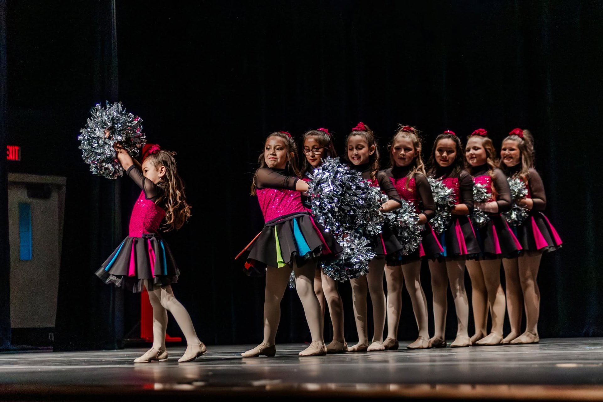 Young pom dancers in a line holding silver poms on stage