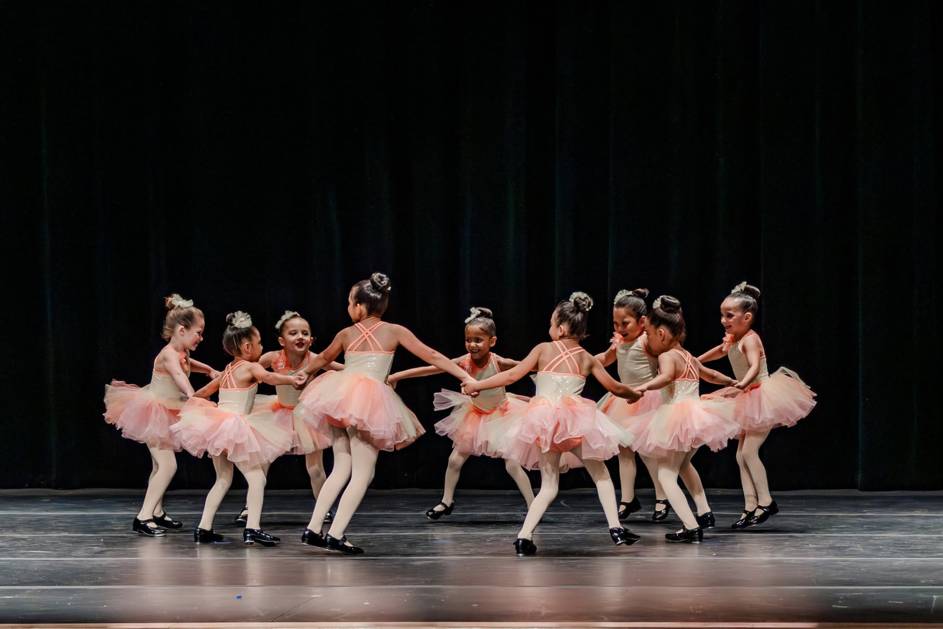 Young tap class holding hands in a circle in peach tutus