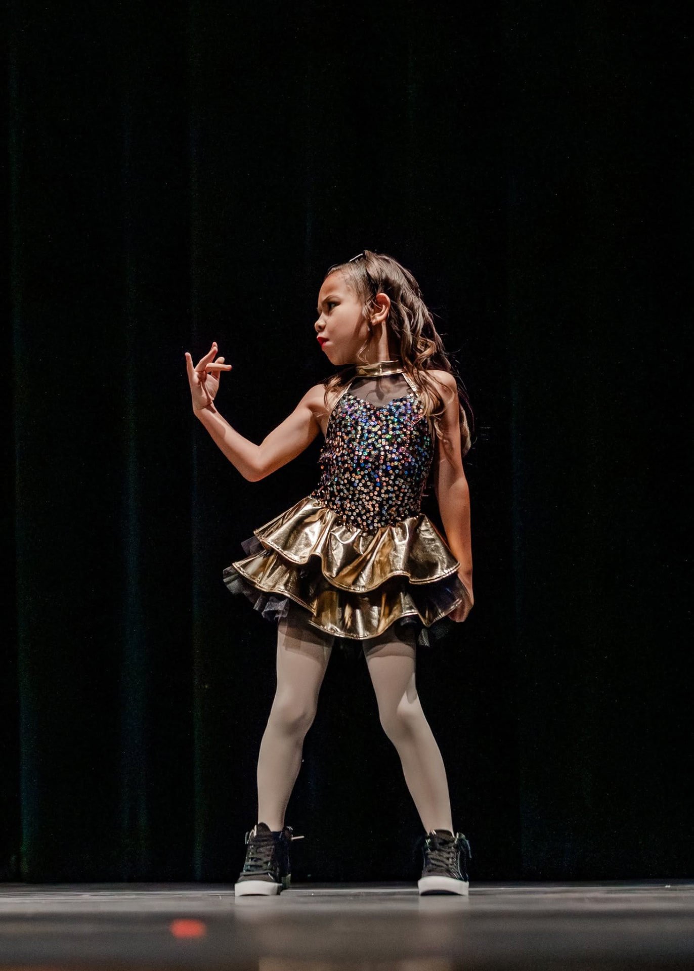 Young dancer in a gold and sequin costume posing on stage