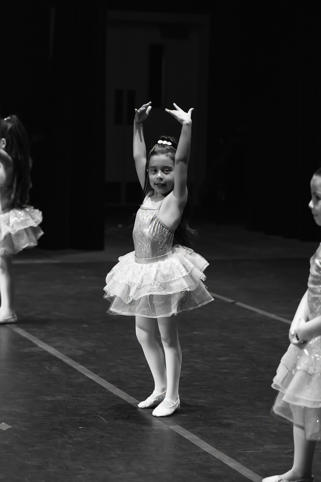 Young ballerina in a sparkling tutu with arms raised overhead on stage