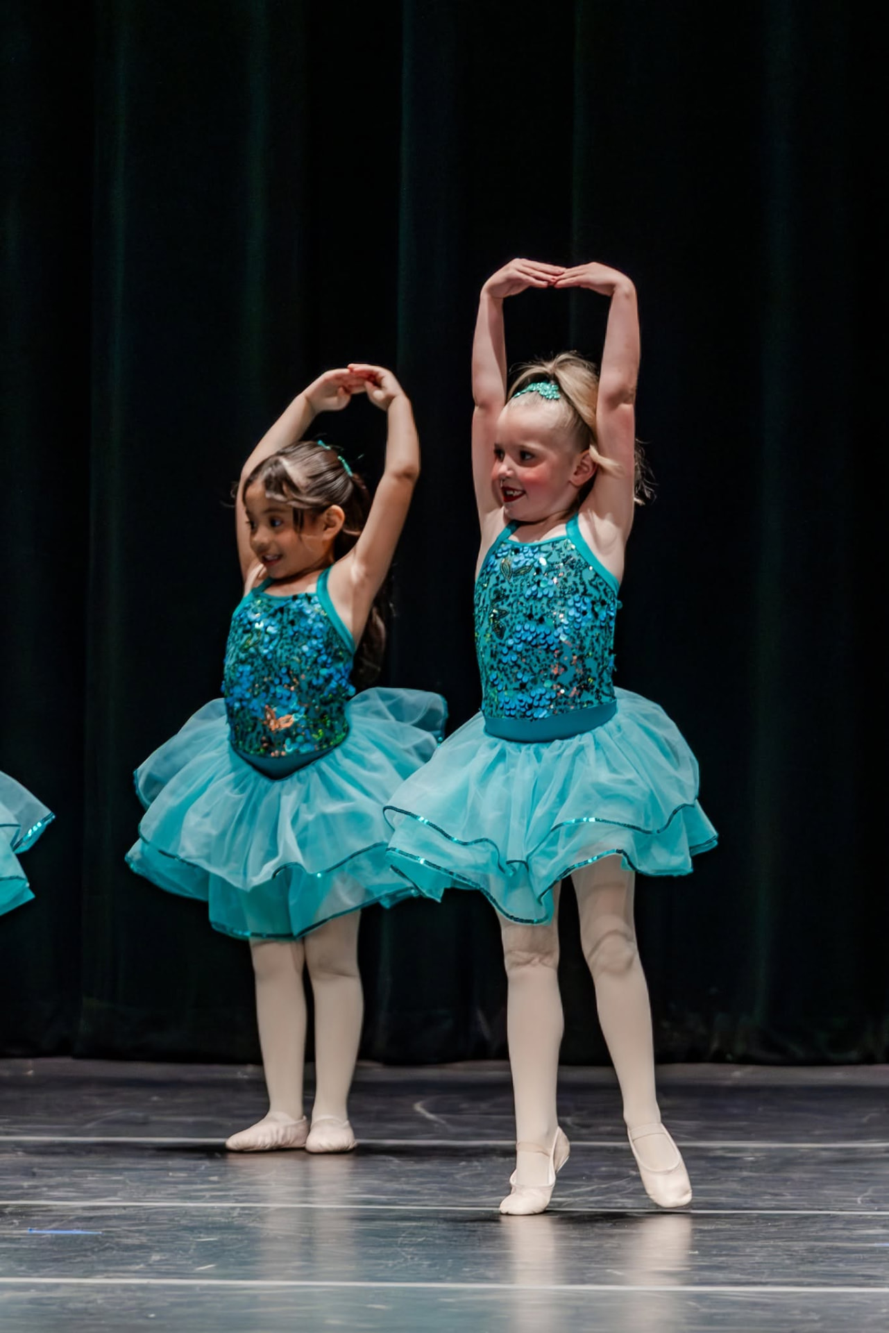 Two young ballerinas in teal tutus posing with arms overhead