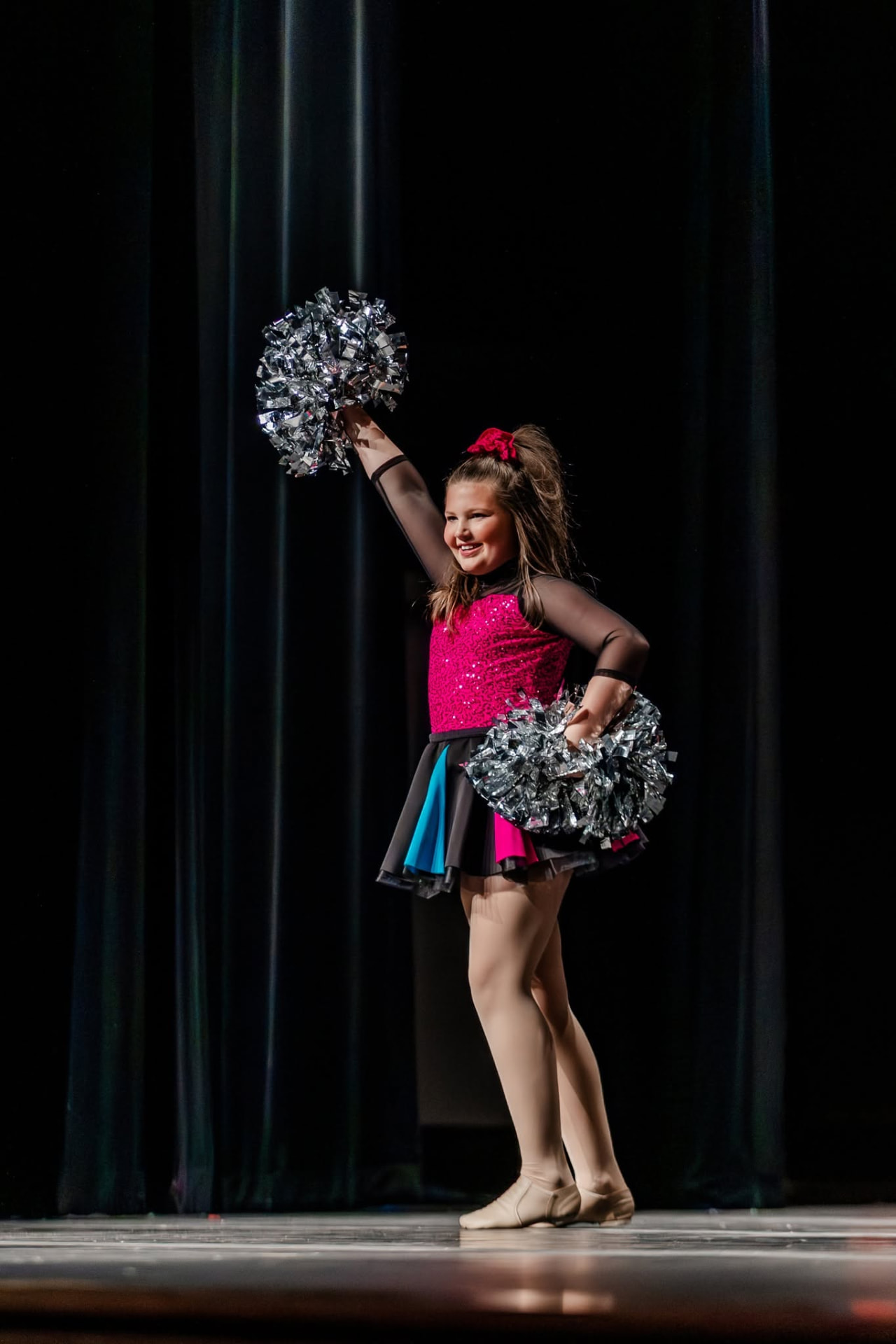 Pom dancer raising a silver pom overhead in a pink costume