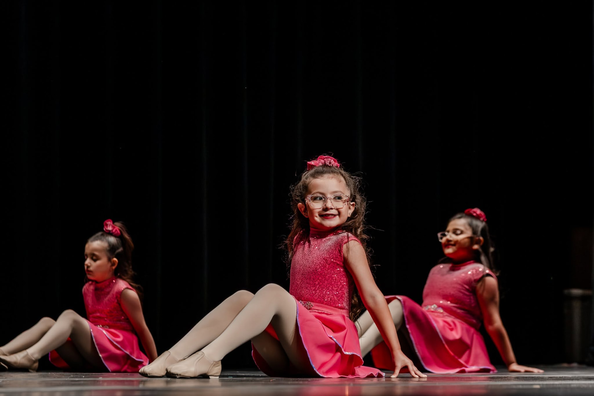 Young dancers in pink sequin costumes seated on stage