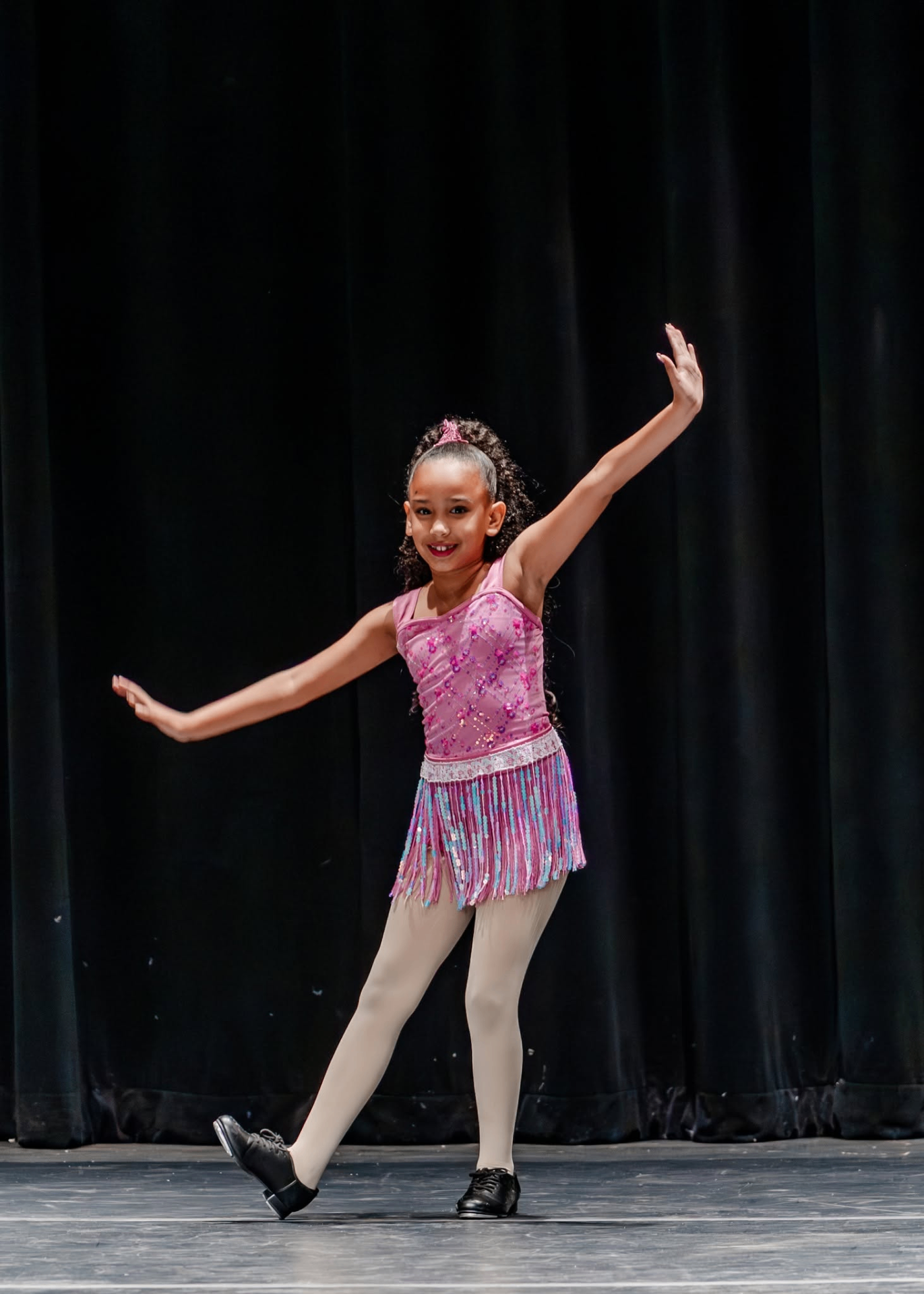 Young Sugar & Spice dancer in a pink sequined fringe costume posing on stage.