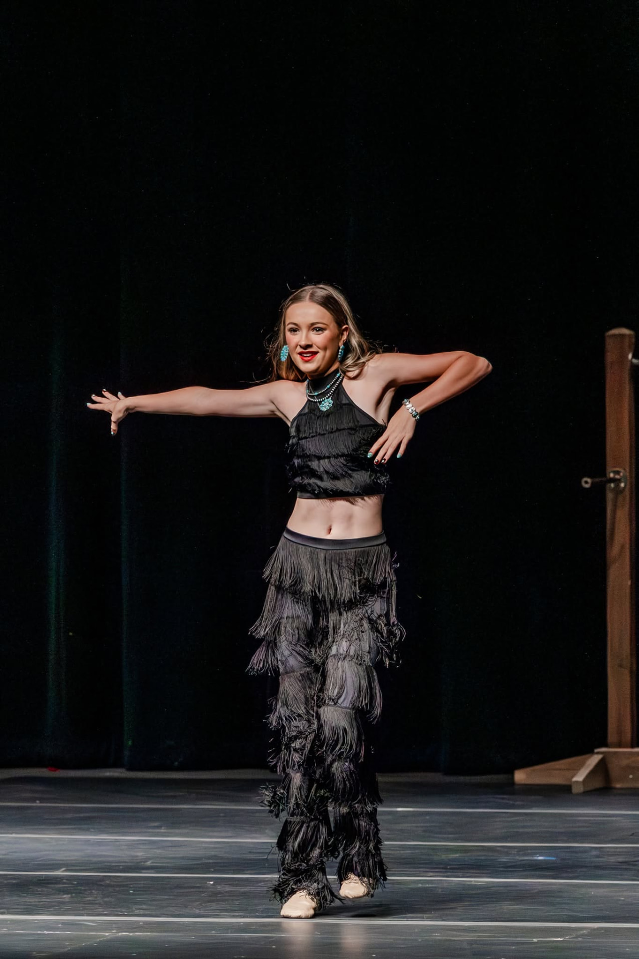 Soloist in black fringe costume with arms extended