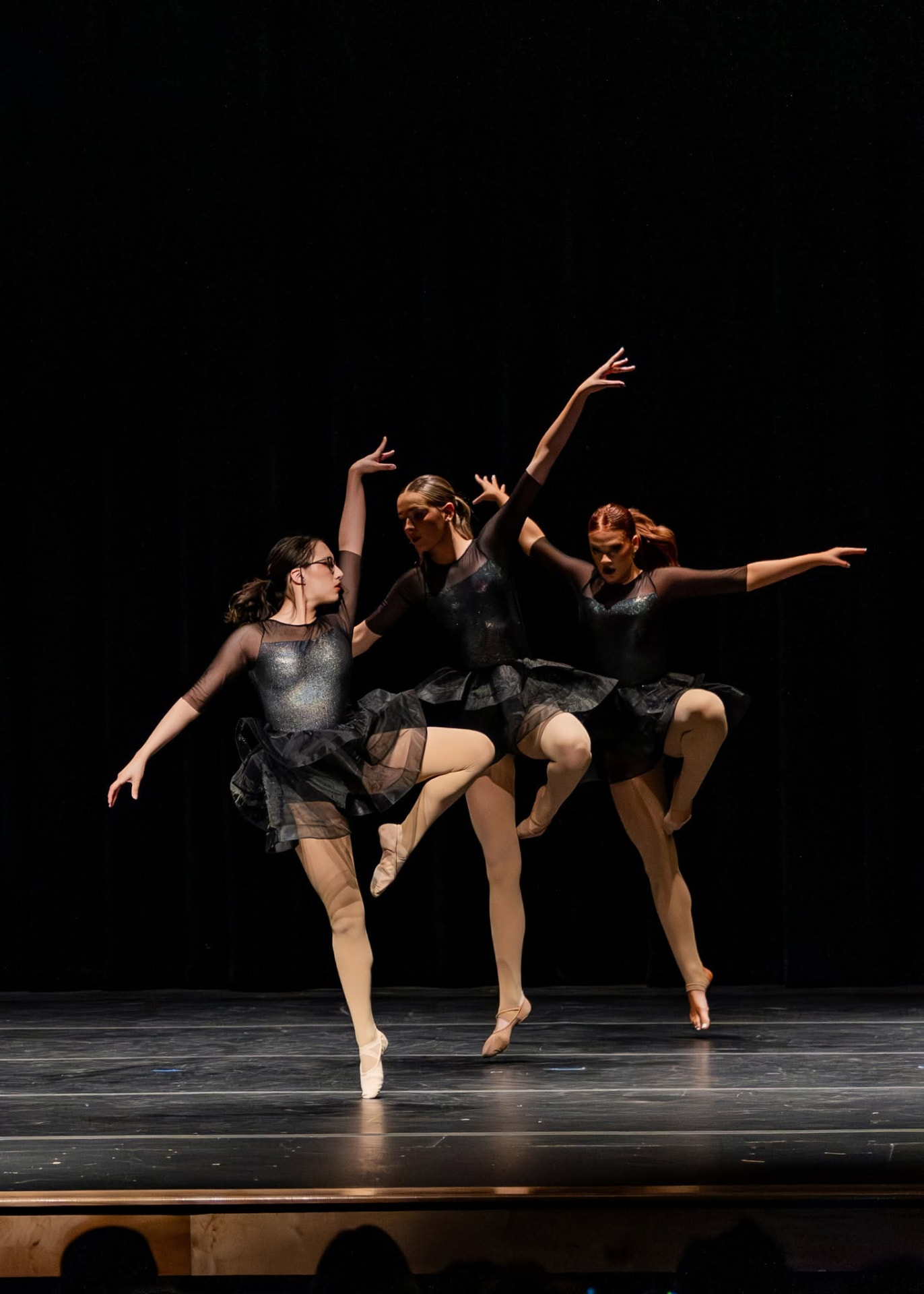 Three dancers in black tutus balancing in passé on stage