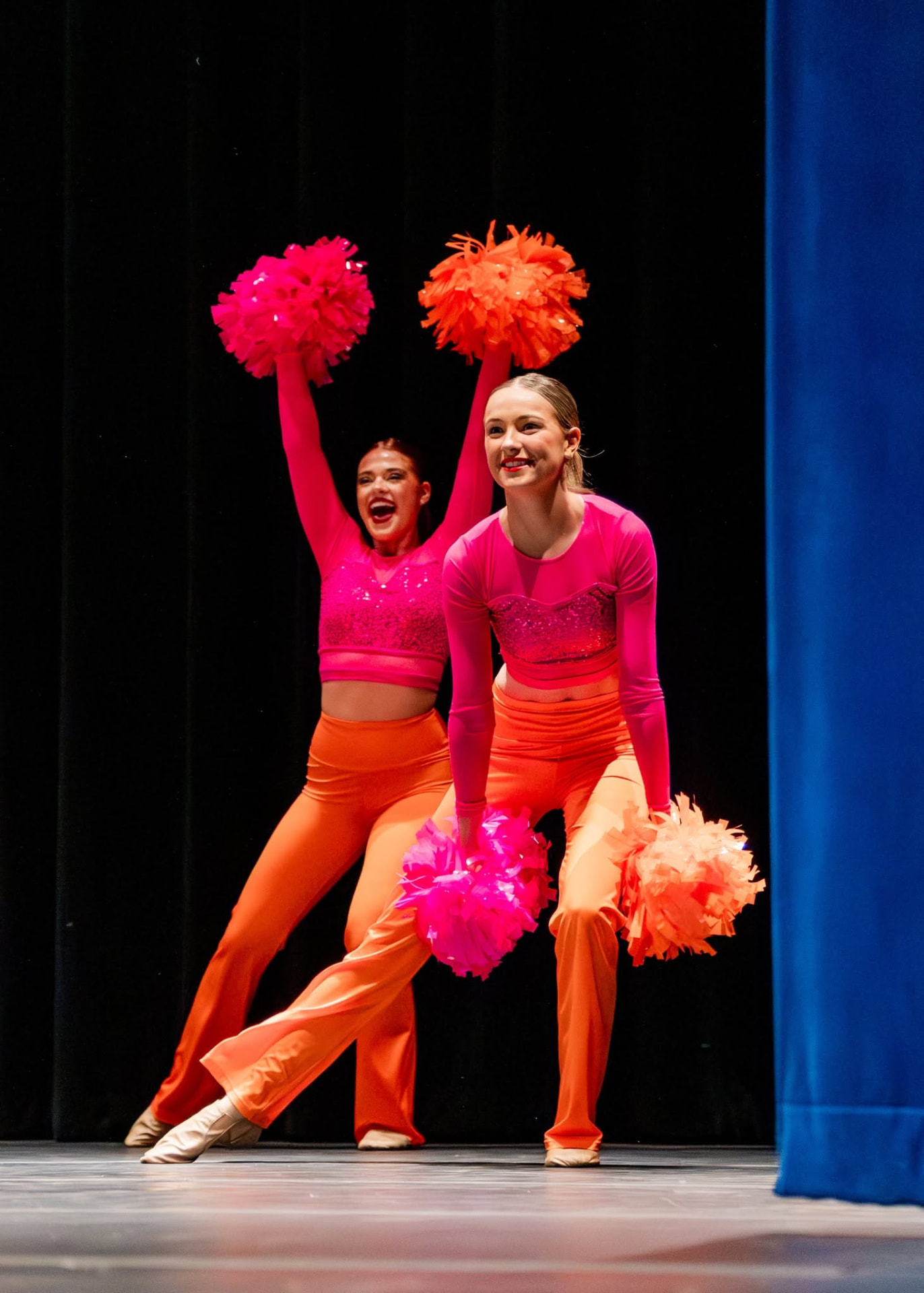 Two pom dancers in pink and orange raising poms overhead