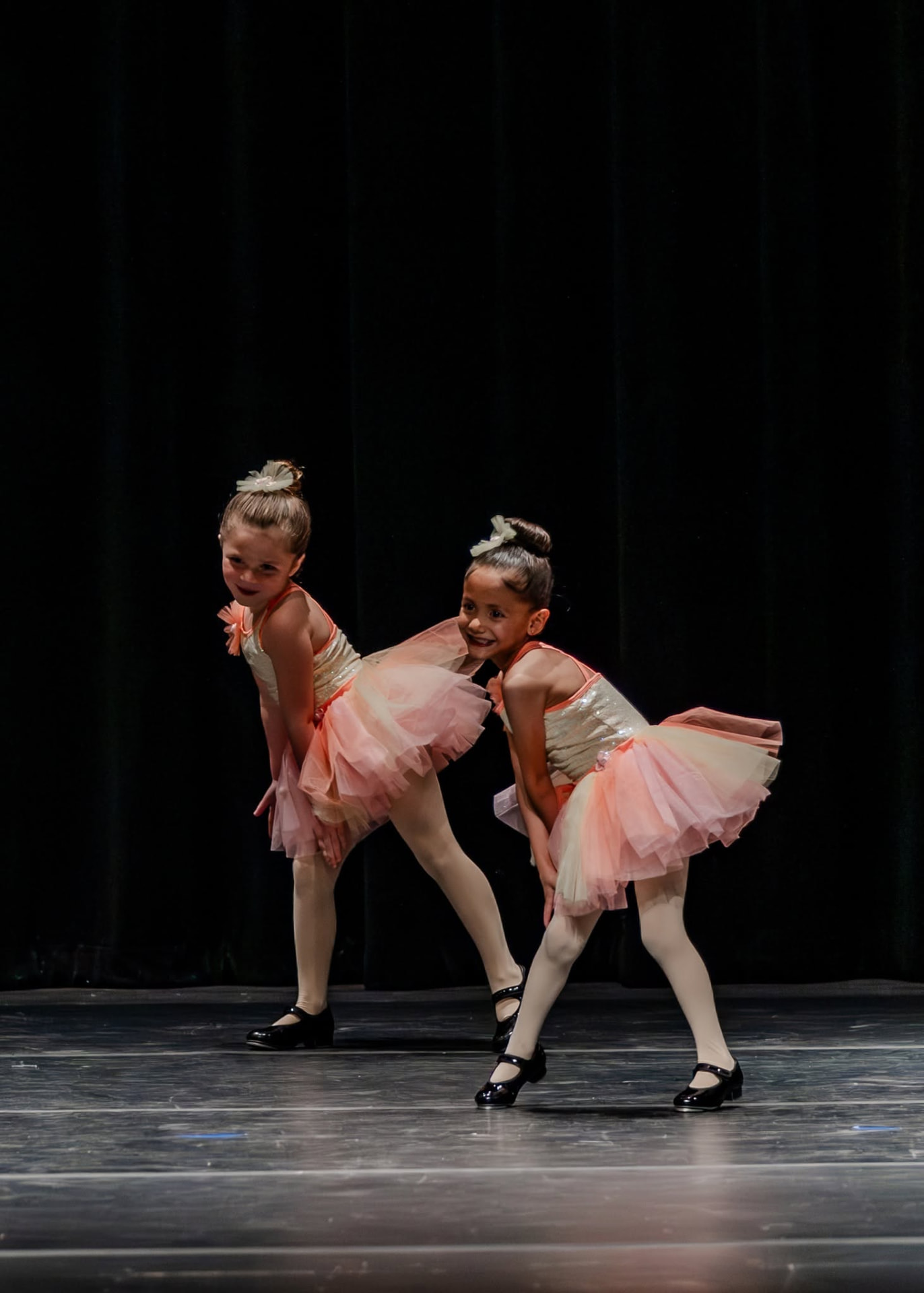 Two tap dancers in peach tutus performing side by side