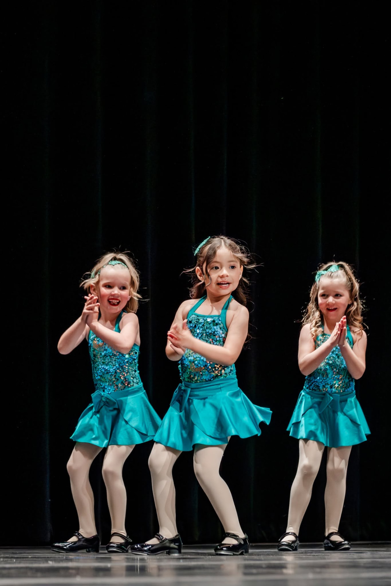 Three young tap dancers in teal sequin costumes