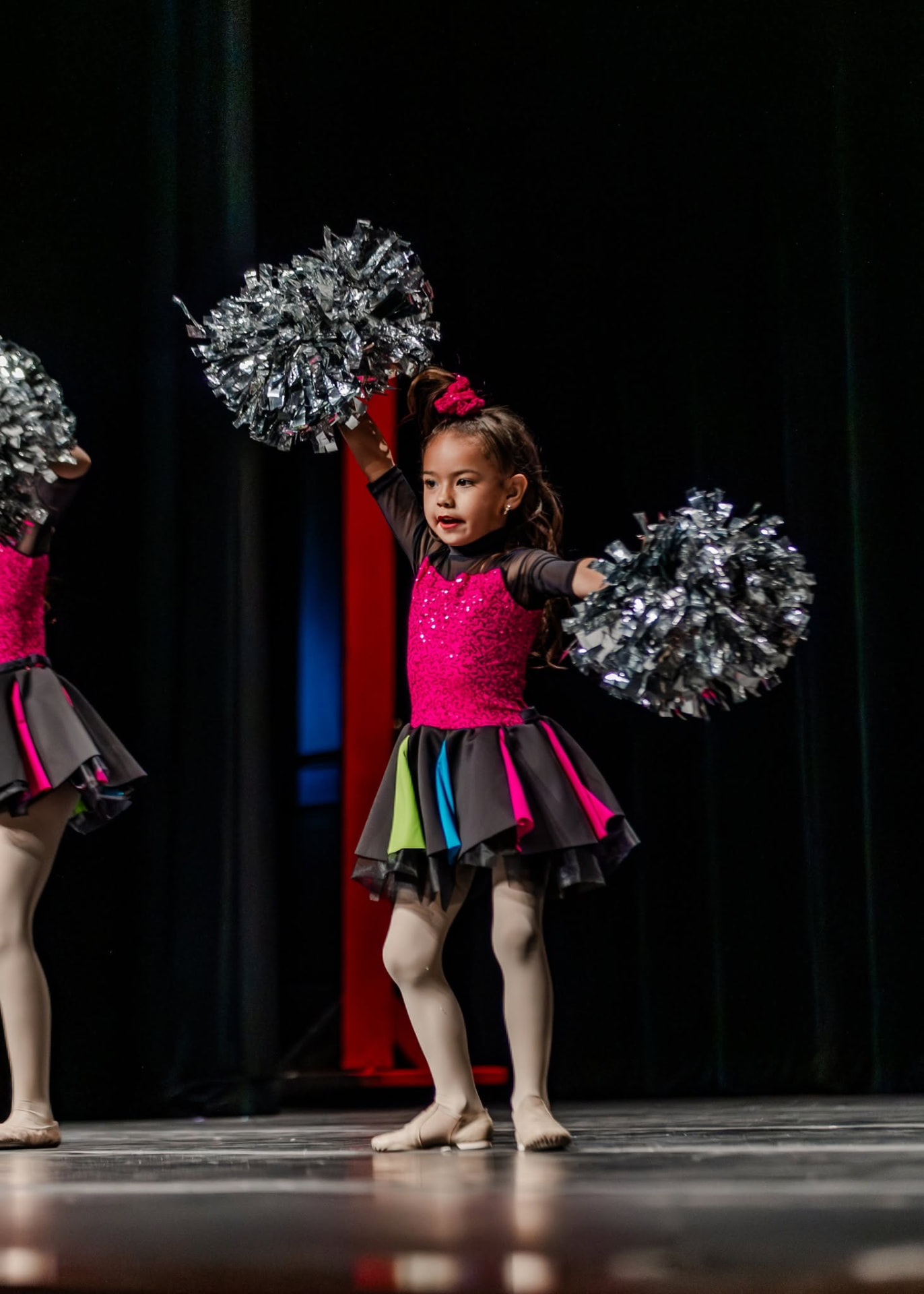 Small dancer raising silver poms above her head