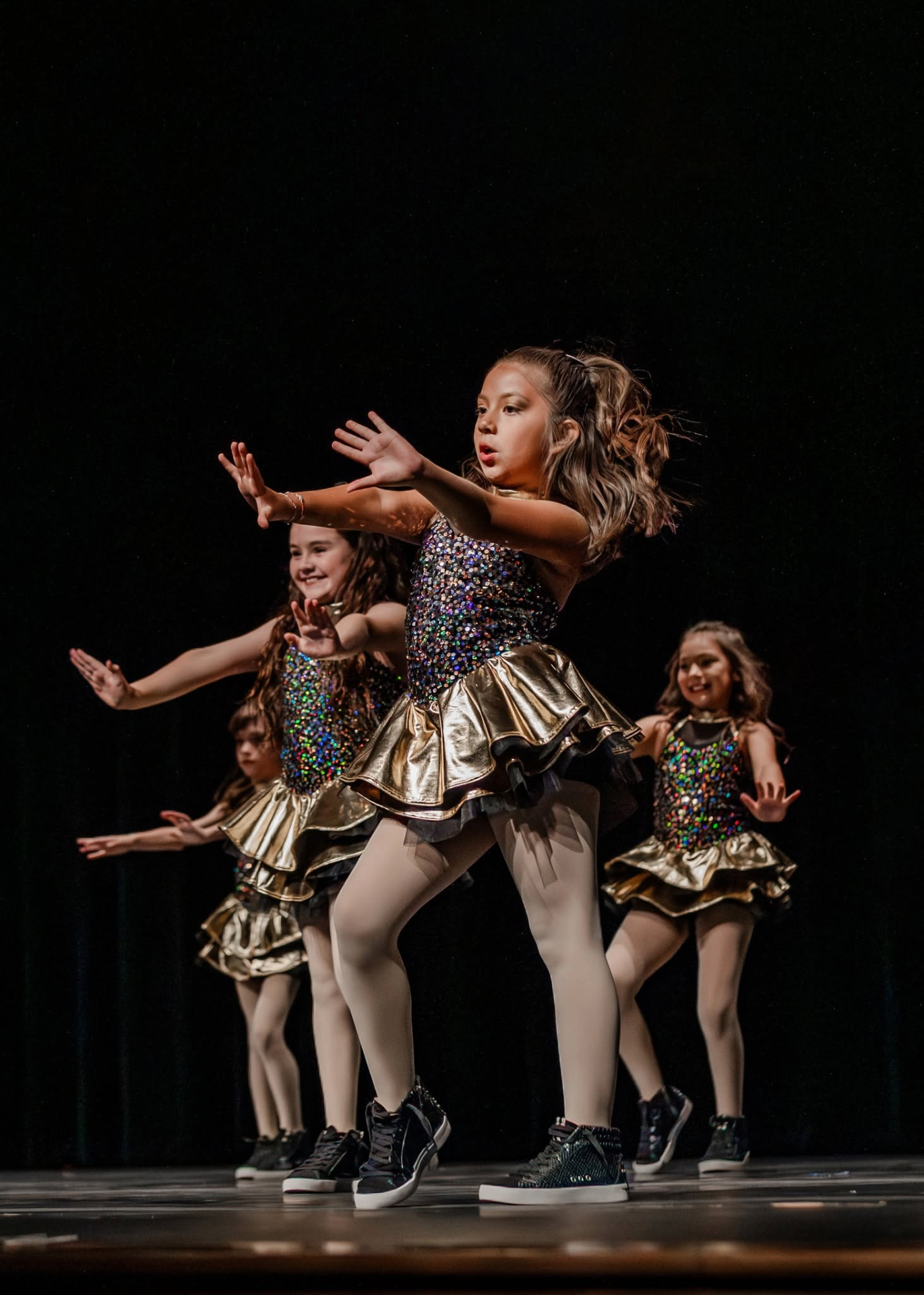 Young hip hop dancers in sparkling black and gold costumes performing on stage.