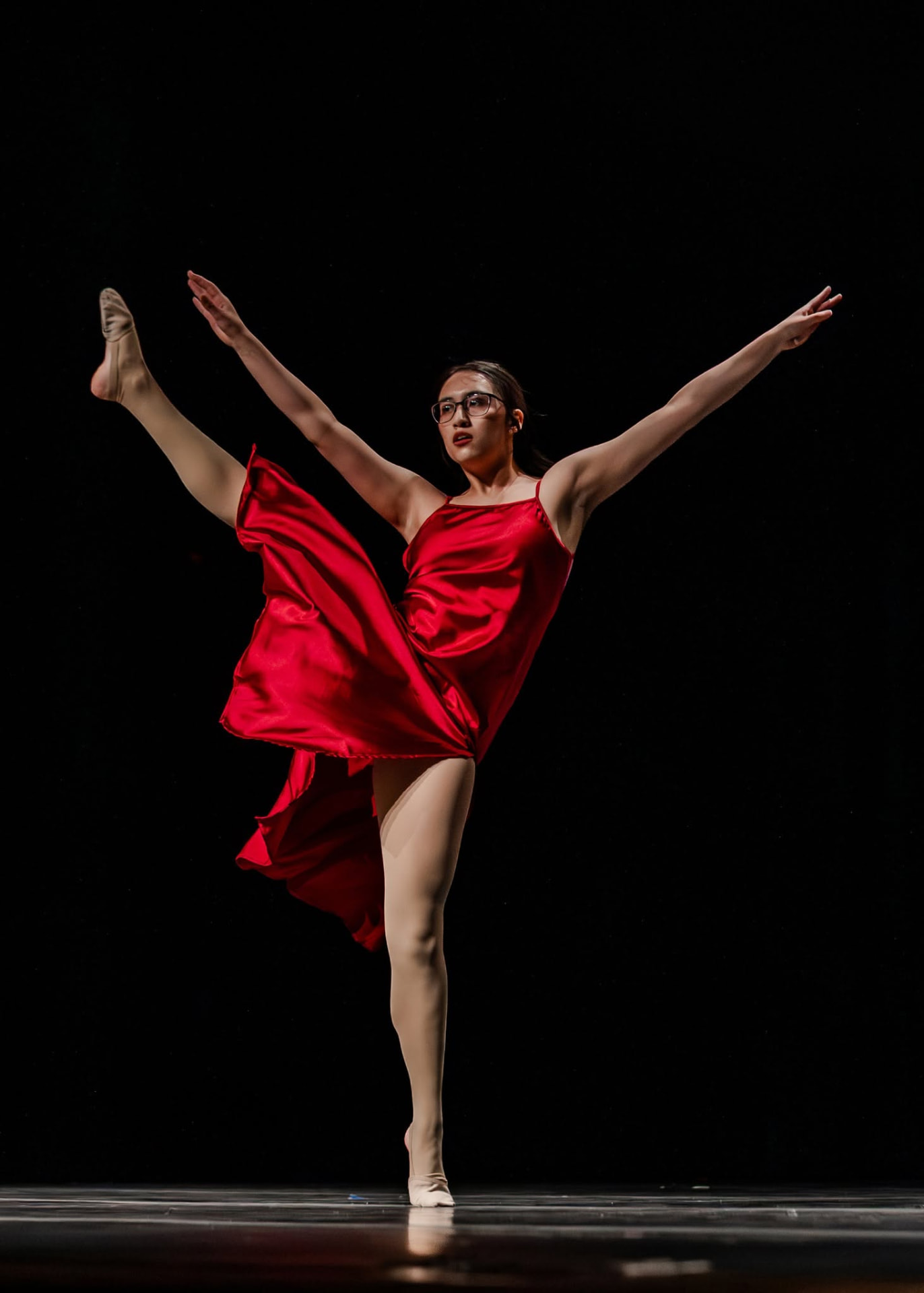 Dancer in a red dress in a high extension beside a set piece