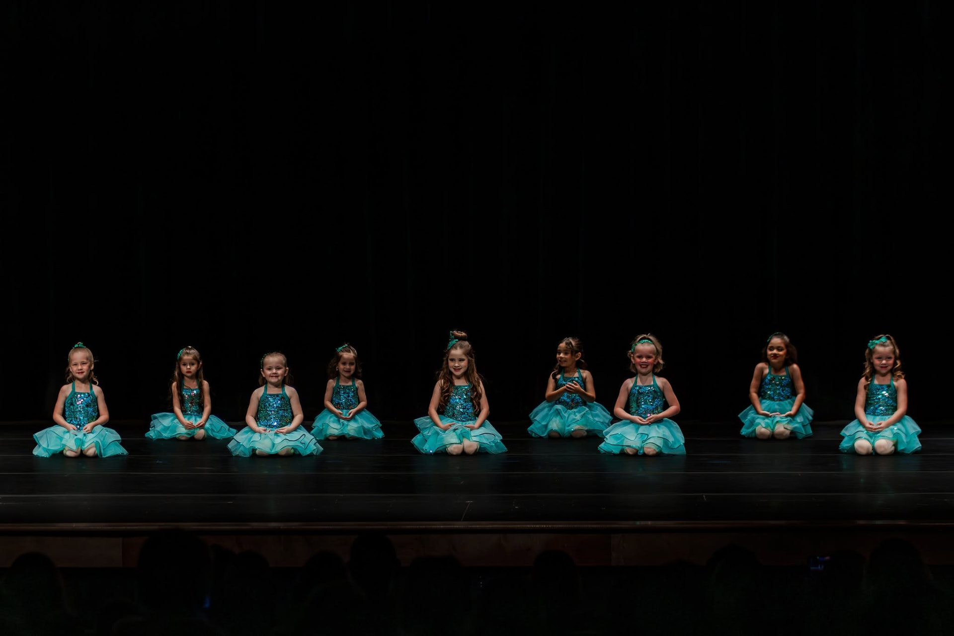 Row of young ballerinas kneeling in teal sequin tutus