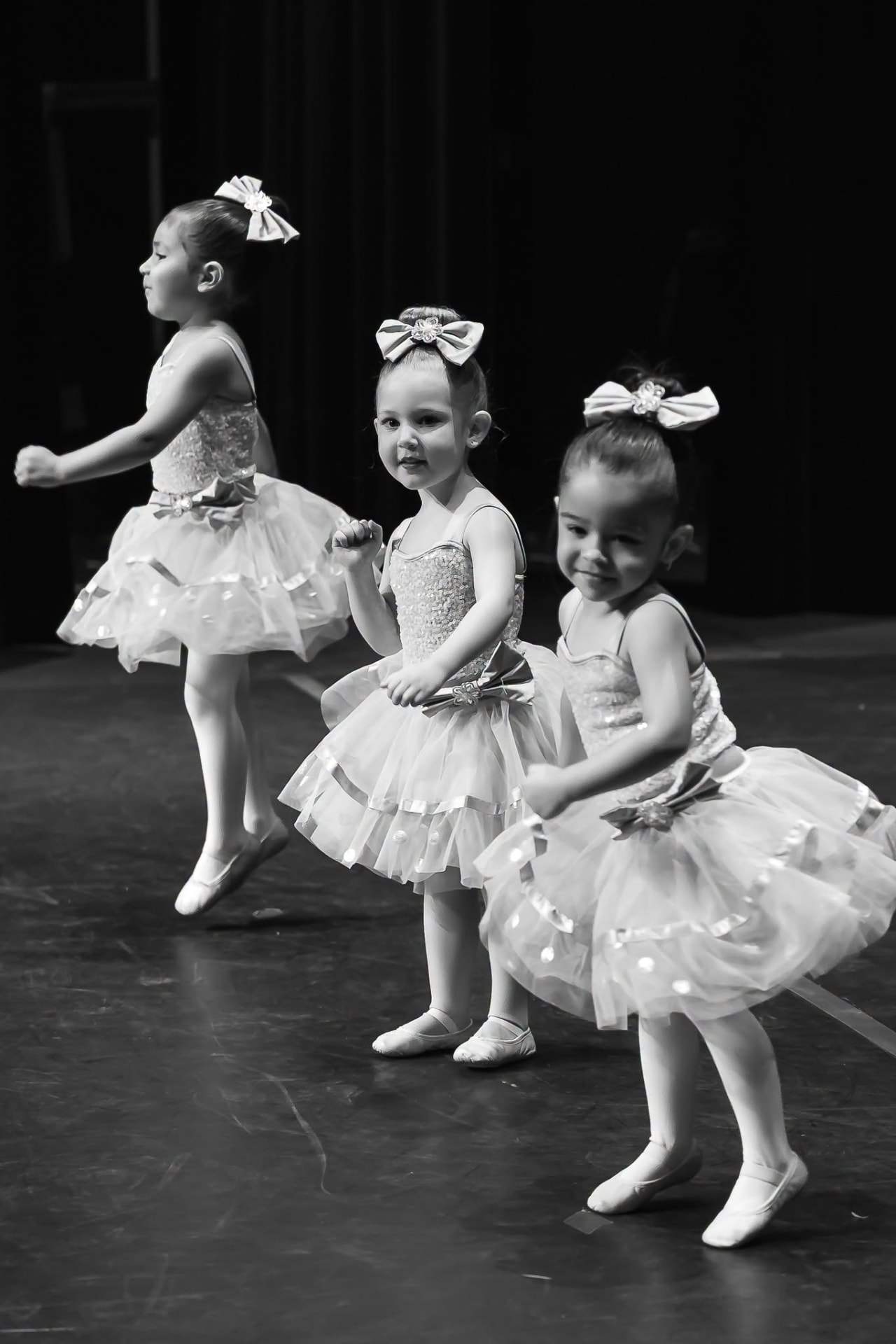 Three toddler ballerinas in sequin tutus with bows in their hair