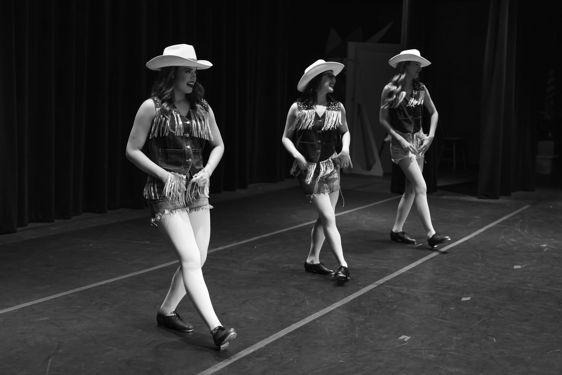 Three tap dancers in denim vests and white cowboy hats performing