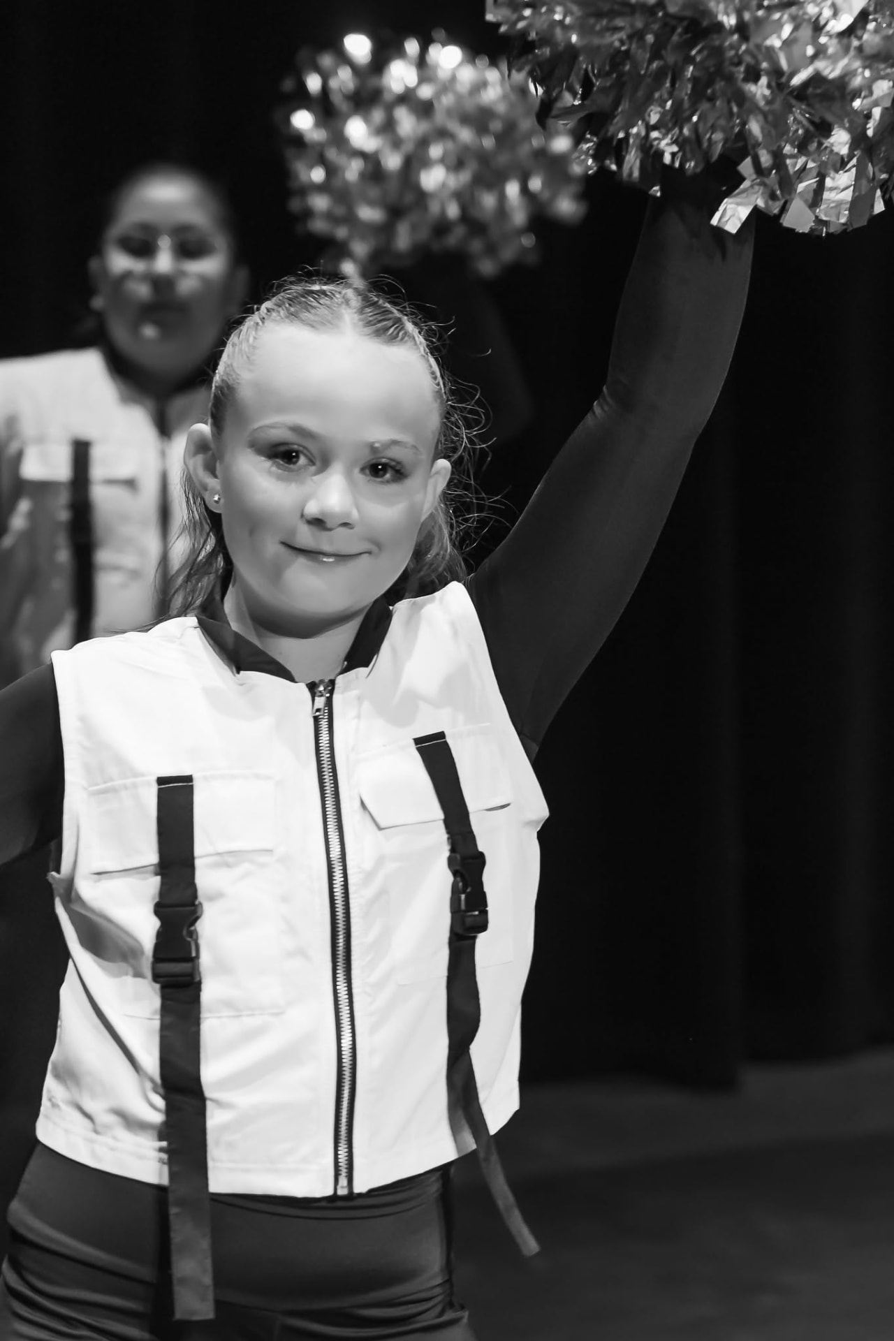 Pom dancer in a white vest raising a pom overhead