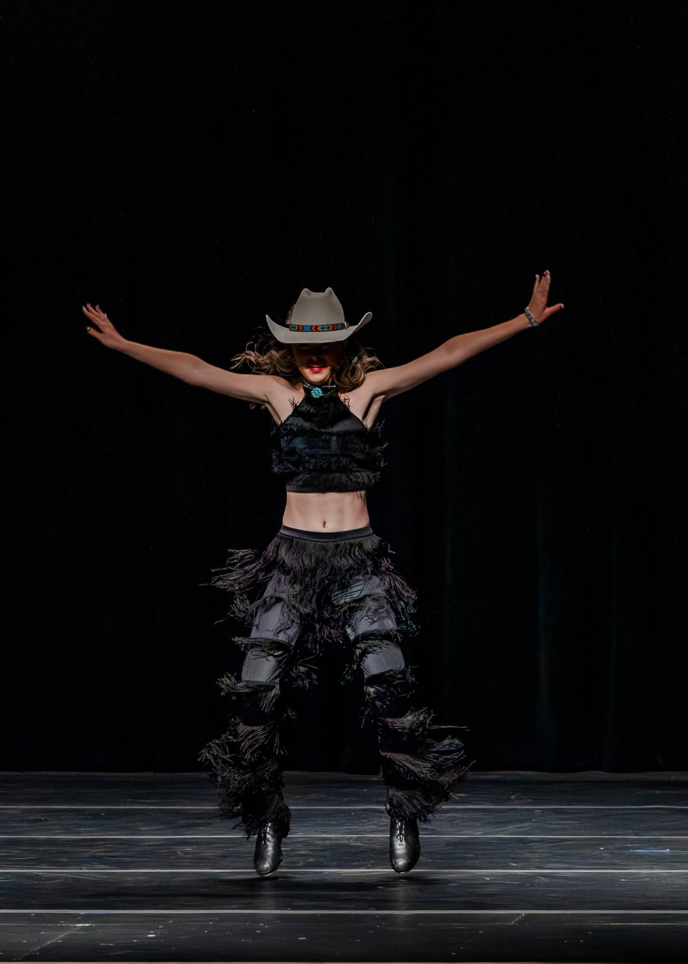 Dancer in a cowboy hat and fringe costume mid-jump