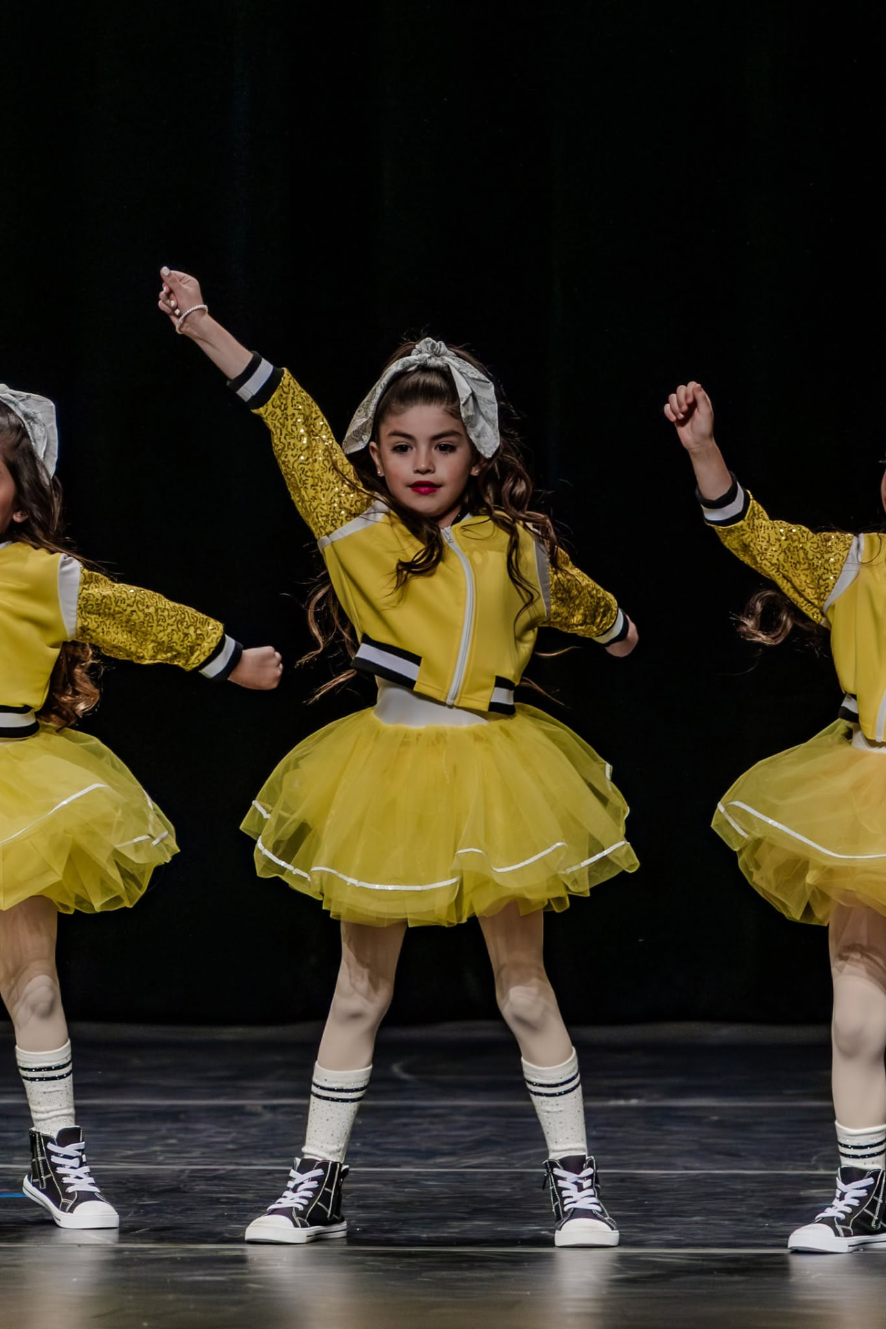 Three dancers in yellow jackets and tulle skirts mid-routine