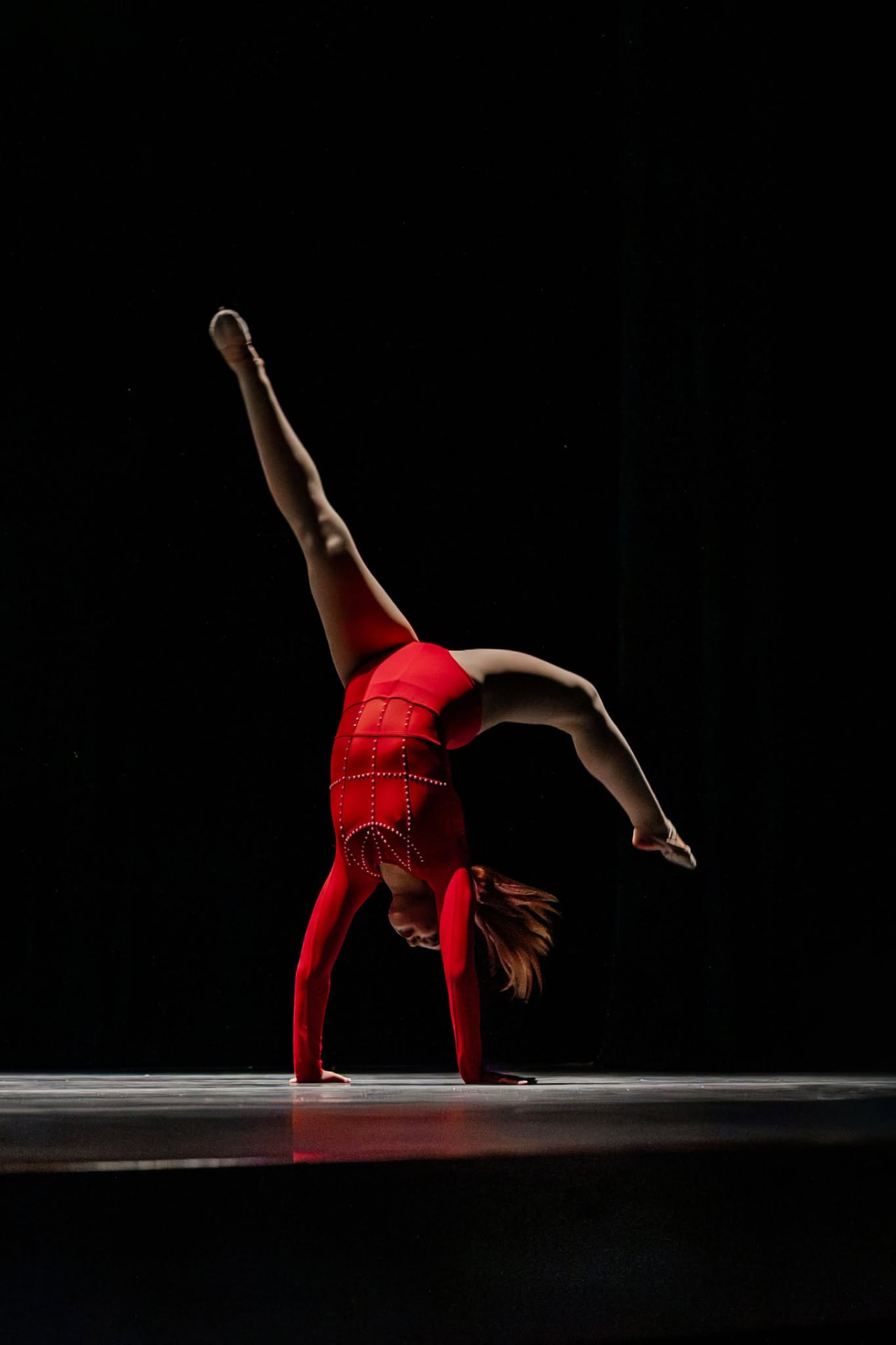 Dancer in a red costume in a one-handed cartwheel on stage
